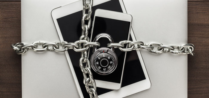 data security concept: computer, tablet, phone bound by metal chain and closed with combination lock on wooden table